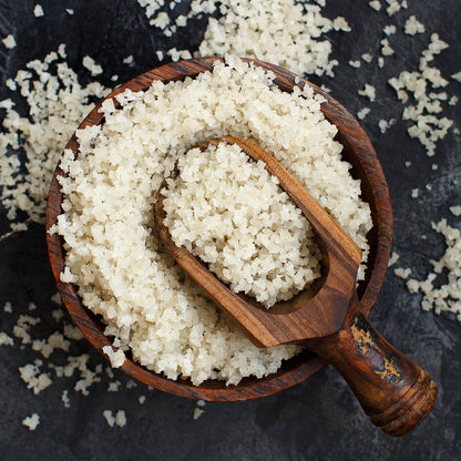 A wooden spoon filled with Celtic Salt sits on top of a wooden bowl filled to the brim with Nano Celtic Sea Salt. 