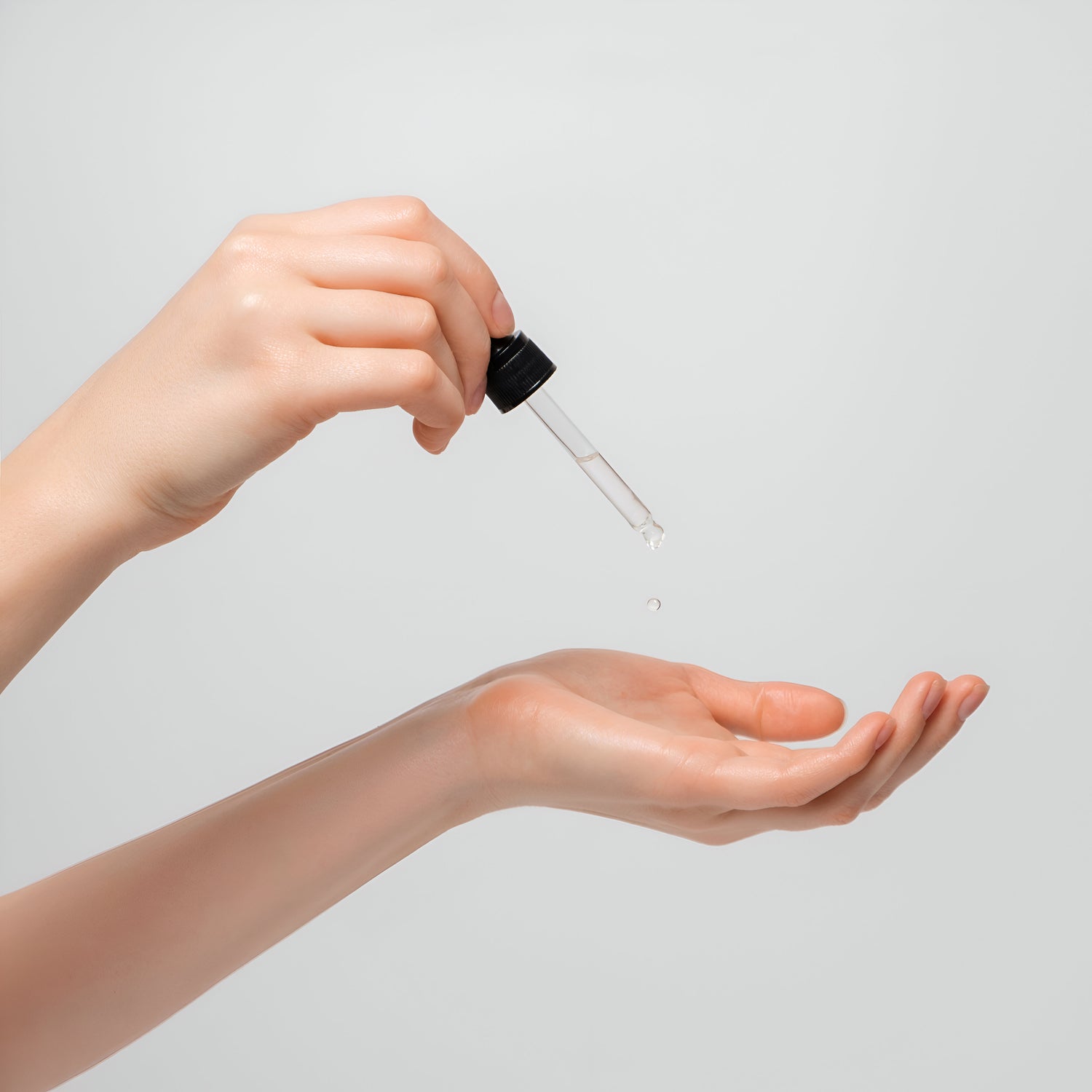 Applying a glass dropper filled with Nano colloidal zinc liquid health supplement to a pair of hands with youthful glowing skin